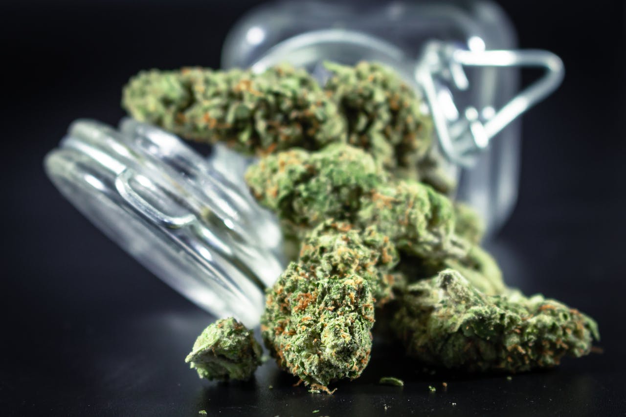 High-quality close-up image of dried cannabis buds spilling out of a glass jar, perfect for various uses.